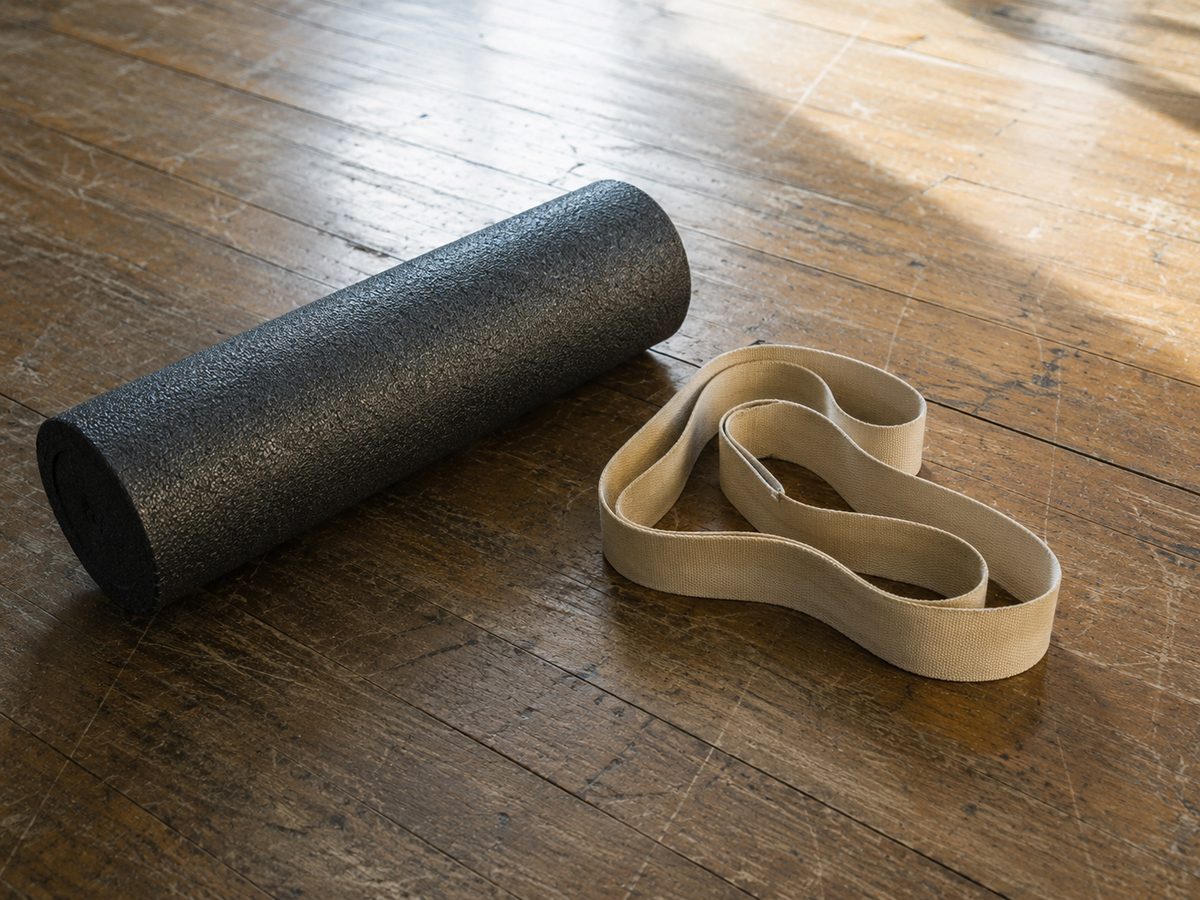 What Is Functional Fascia Fitness, and Why Do Most Workouts Ignore It? A black foam roller and a loosely coiled fabric resistance band lying on a scuffed wooden gym floor in daylight